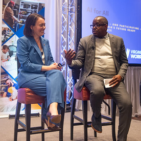 Two panelists seated on stage during a discussion at a conference, with “AI for All” and “Virginia Works” banners visible in the background.