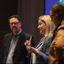 Three panelists participate in a conference discussion on stage, with one speaker addressing the audience while the others listen.